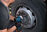 Seseorang yang mengenakan perlengkapan keselamatan menggunakan kunci pas benturan untuk mengencangkan baut pada roda truk.