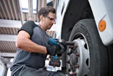 Seseorang yang mengenakan perlengkapan keselamatan menggunakan kunci pas benturan tanpa kabel pada roda truk.