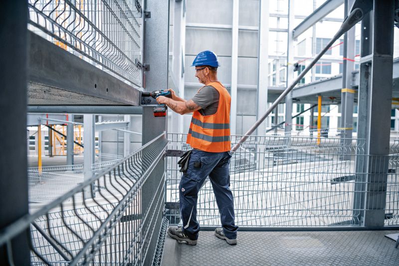 Orang yang mengenakan peralatan keselamatan menggunakan kunci pas benturan pada balok baja di lokasi konstruksi.