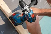Seseorang menggunakan bor tanpa kabel untuk mengencangkan sekrup ke balok kayu.