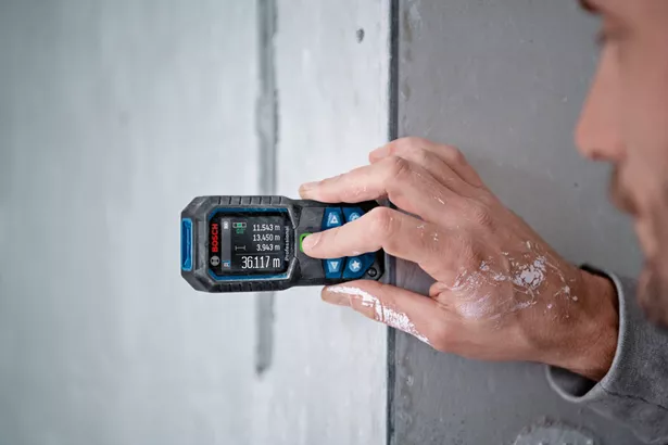 GLM 50-23 G Orang mengukur jarak dinding dengan laser pengukur, cat terlihat di tangannya.