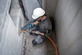 Seseorang yang mengenakan peralatan keselamatan menggunakan senapan panas tanpa kabel untuk bekerja pada kabel oranye.