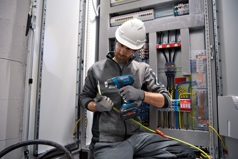 Seseorang yang mengenakan perlengkapan keselamatan menggunakan senapan panas tanpa kabel pada kabel listrik.