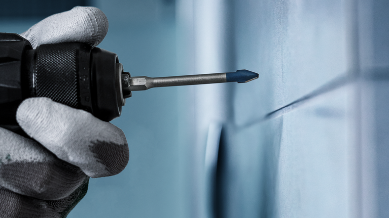 Seseorang yang mengenakan peralatan keselamatan mengebor lubang di dinding keramik.
