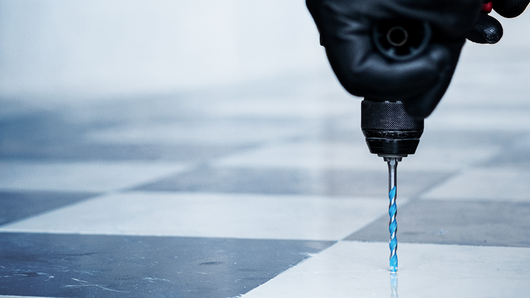 Orang yang mengenakan peralatan keselamatan mengebor lantai keramik.