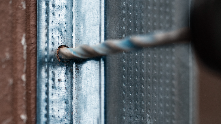 Mata bor membuat lubang di dinding rangka logam.