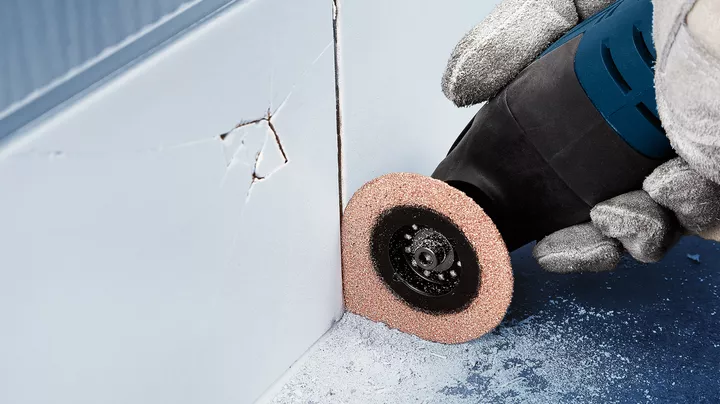 Object #200360570: 2793193_web_002 Seorang pekerja yang mengenakan perlengkapan keselamatan menggunakan alat putar untuk memotong drywall di dekat sudut.