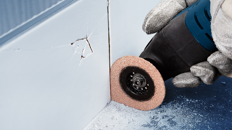 Orang yang mengenakan peralatan keselamatan menggunakan alat putar untuk menggiling di dekat sudut dinding.