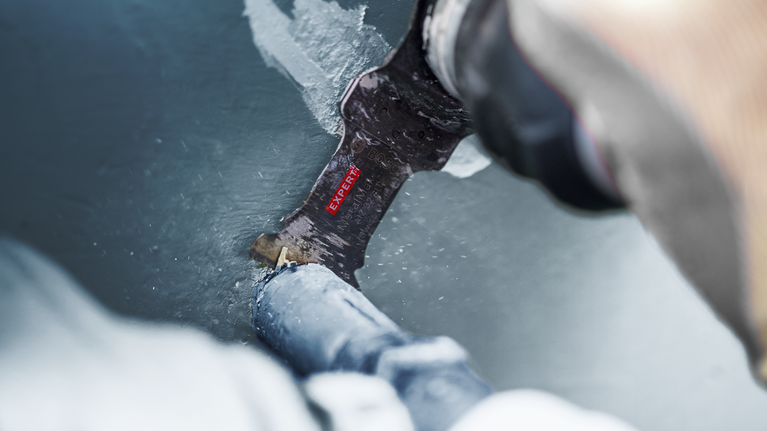 Seseorang menggunakan mata pisau alat multifungsi untuk memotong pipa plastik.