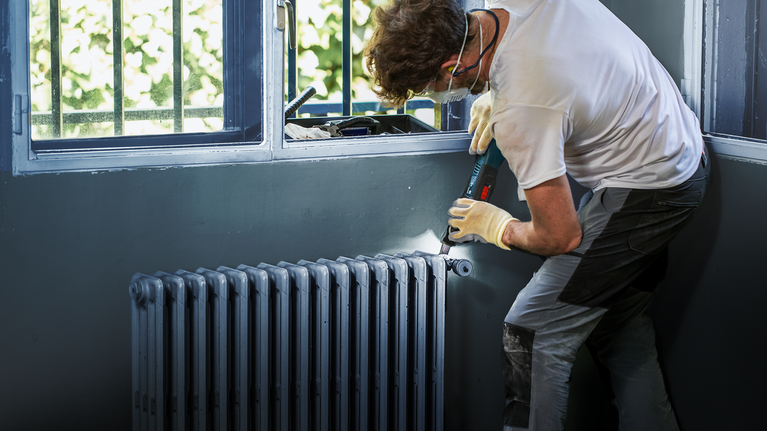 Orang yang mengenakan peralatan keselamatan menggunakan bor tanpa kabel untuk memasang radiator.
