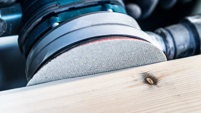 Mesin amplas orbital menghaluskan permukaan papan kayu.