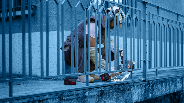 Seseorang yang mengenakan peralatan keselamatan menggunakan mesin gerinda untuk memotong pagar logam.