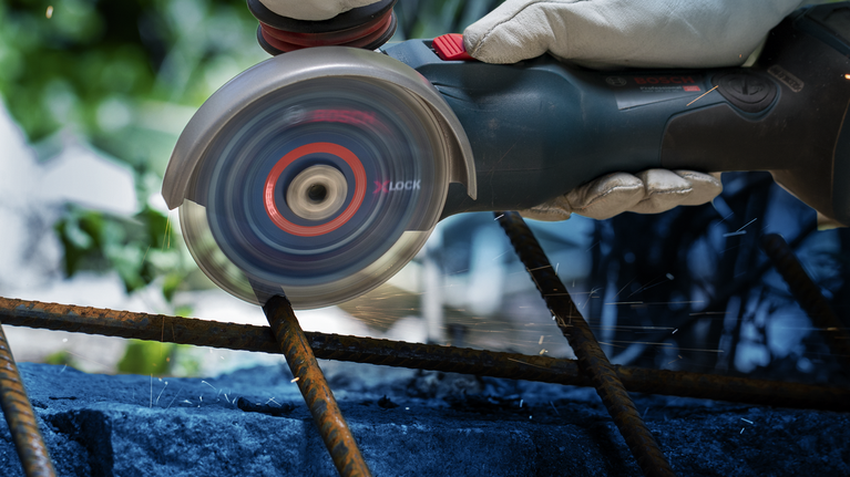 Seseorang yang mengenakan perlengkapan keselamatan menggunakan gerinda sudut untuk memotong besi beton.