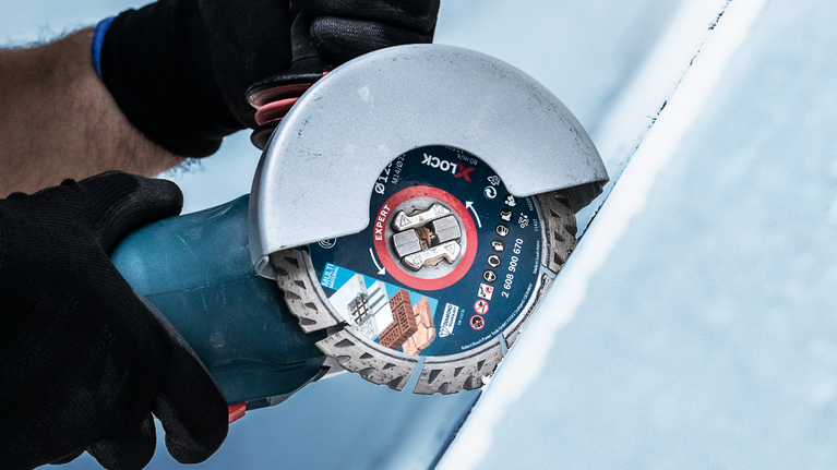 Seseorang yang mengenakan perlengkapan keselamatan menggunakan mesin gerinda sudut untuk memotong ubin.