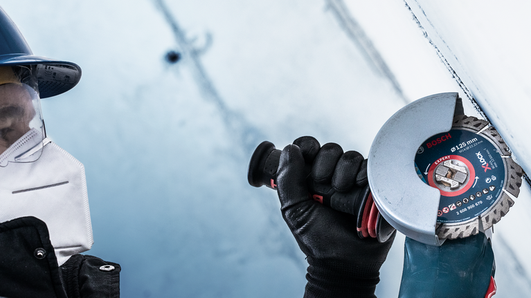 Seseorang yang mengenakan peralatan keselamatan menggunakan mesin gerinda sudut untuk memotong permukaan logam.