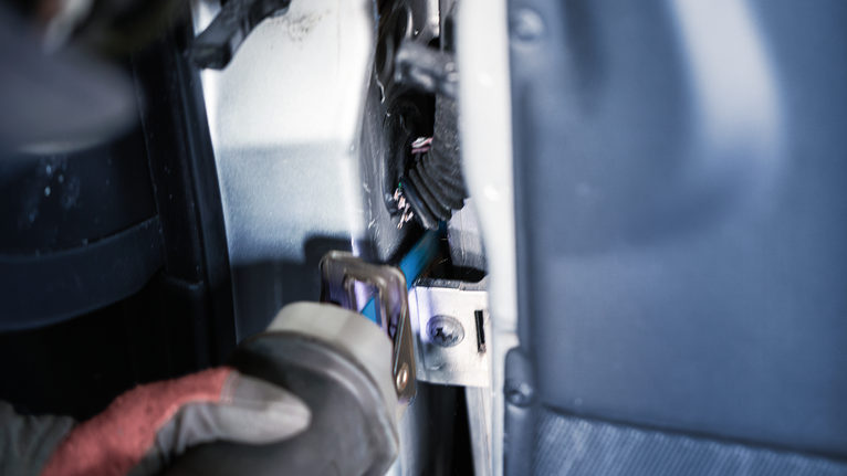 Seseorang yang mengenakan peralatan keselamatan memotong logam di dalam ruang sempit menggunakan gergaji bolak-balik.