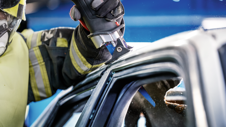 Seseorang yang mengenakan perlengkapan keselamatan menggunakan alat listrik untuk memotong rangka mobil.