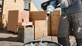 Seseorang yang mengenakan peralatan keselamatan mencampur mortar dalam ember dengan alat pengaduk.