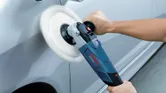 Seseorang menggunakan alat pemoles untuk memoles permukaan pintu mobil.