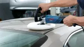 Seseorang memoles atap mobil dengan alat poles listrik di garasi dalam ruangan.