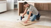 Seseorang mengebor papan kayu di lantai dapur yang sedang direnovasi.
