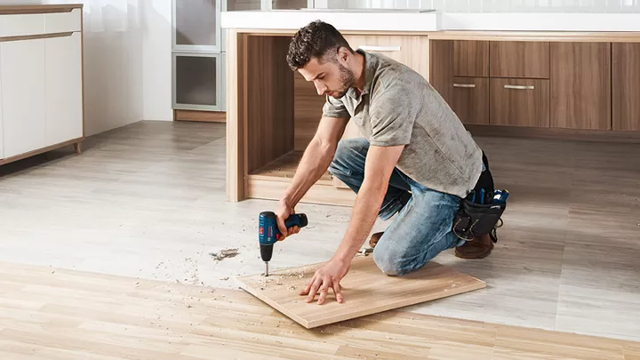 GSR 120-LI Seseorang mengebor papan kayu di lantai dapur yang sedang direnovasi.