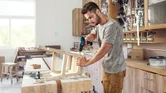 Seseorang merakit kursi kayu menggunakan bor tanpa kabel di bengkel.