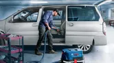 Seseorang membersihkan bagian dalam mobil dengan penyedot debu di samping kereta peralatan di garasi.