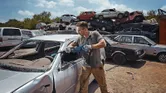 Seseorang yang mengenakan peralatan keselamatan memotong pintu mobil dengan gergaji bolak-balik di tempat barang rongsokan.