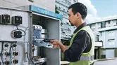 Seseorang yang mengenakan peralatan keselamatan menggunakan obeng tanpa kabel pada panel listrik.