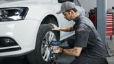 Seseorang yang mengenakan perlengkapan keselamatan menggunakan kunci pas benturan tanpa kabel untuk mengencangkan baut roda pada mobil.