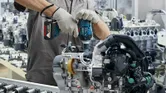 Seseorang yang mengenakan perlengkapan keselamatan menggunakan kunci pas benturan tanpa kabel pada rakitan mesin.