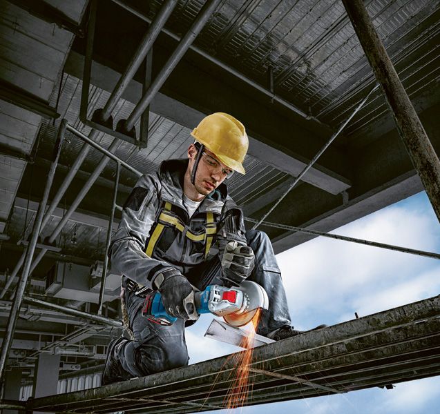 Seseorang yang mengenakan peralatan keselamatan menggunakan penggiling sudut tanpa kabel untuk memotong logam.