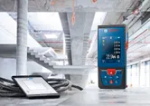 Pengukur laser dan tablet yang menampilkan pengukuran pada permukaan beton di lokasi konstruksi.
