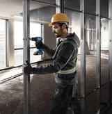 Seseorang yang mengenakan perlengkapan keselamatan mengencangkan kancing logam dengan bor tanpa kabel.