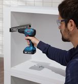 Orang yang mengenakan peralatan keselamatan menggunakan bor tanpa kabel untuk memasang slide laci di lemari.