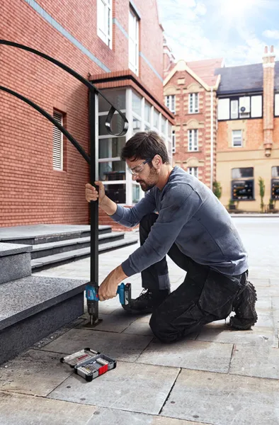 Seseorang yang mengenakan peralatan keselamatan mengebor anak tangga batu dan memasang pegangan tangan dari logam.