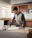 Orang yang mengenakan peralatan keselamatan mengebor papan kayu di ruang kerja dapur.