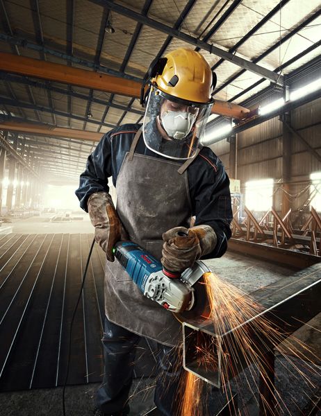Seseorang yang mengenakan peralatan keselamatan menggiling logam, menghasilkan percikan terang di pabrik.