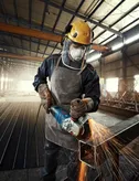 Seseorang yang mengenakan peralatan keselamatan menggiling logam, menghasilkan percikan terang di pabrik.