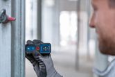 Orang yang mengenakan perlengkapan keselamatan menggunakan pengukur laser untuk memeriksa jarak pada sinar logam.