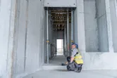 Seseorang yang mengenakan perlengkapan keselamatan menggunakan pengukur laser untuk memeriksa jarak dalam struktur beton.