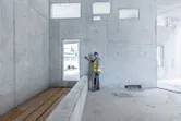 Seseorang yang mengenakan perlengkapan keselamatan menggunakan sinar laser pada dinding beton.