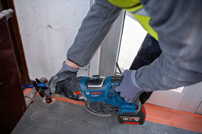 Seseorang yang mengenakan peralatan keselamatan menggunakan gergaji bolak-balik untuk memotong logam di dekat kusen pintu.