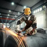 Seseorang yang mengenakan peralatan keselamatan menggiling logam, sehingga menimbulkan percikan api di lingkungan industri.