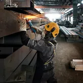 Seseorang yang mengenakan peralatan keselamatan menggiling sinar logam, sehingga menghasilkan percikan terang.