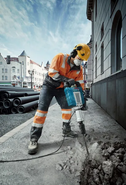 Seseorang yang mengenakan peralatan keselamatan merusak trotoar dengan pemutus arus listrik di jalan kota.