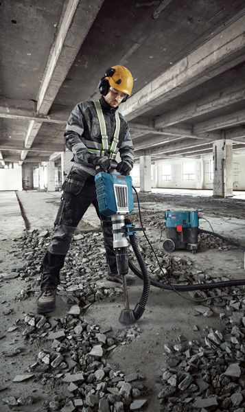 Seseorang yang mengenakan perlengkapan keselamatan menggunakan pemutus arus untuk menghancurkan lantai beton.