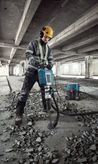 Seseorang yang mengenakan perlengkapan keselamatan menggunakan pemutus arus untuk menghancurkan lantai beton.