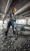 Seseorang yang mengenakan perlengkapan keselamatan menggunakan pemutus arus untuk menghancurkan lantai beton.